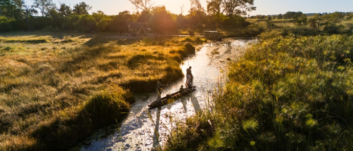 A mokor moves through a Okavango Delta waterway at sunset